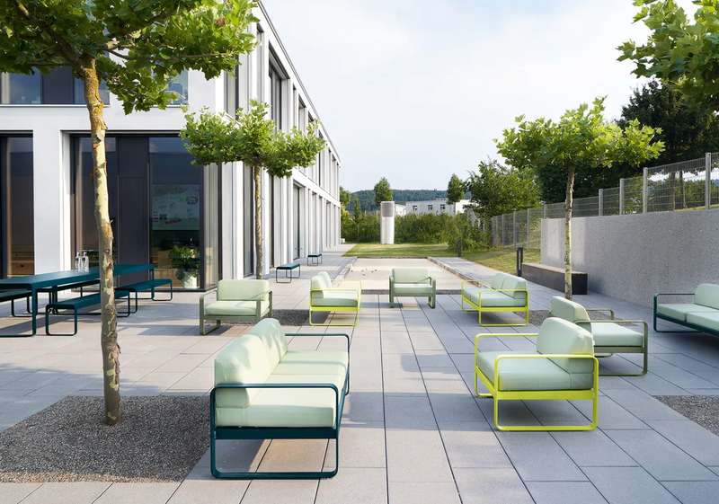 Load image into Gallery viewer, Outdoor Fermob Bellevie 2-seater sofa with colorful cushions, modern design, and wooden legs on a patio.