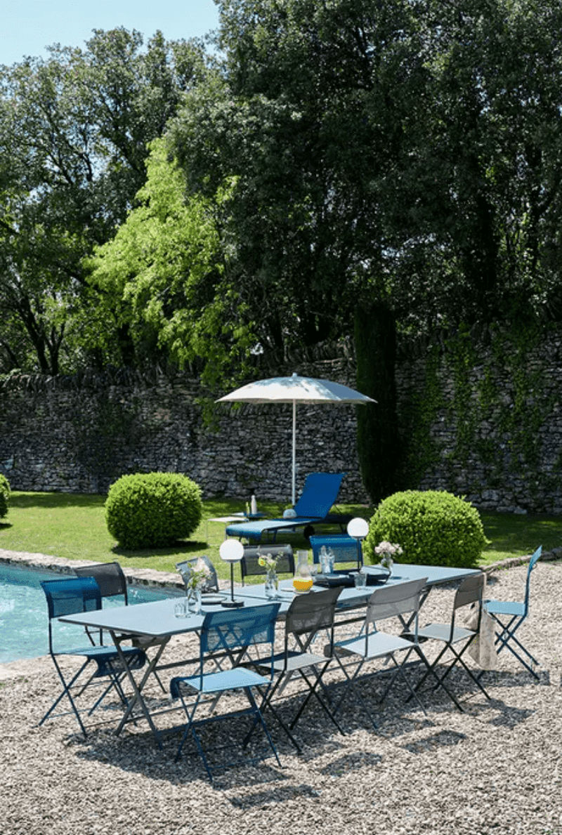 Load image into Gallery viewer, Fermob Caractère outdoor foldable metal table, 128 x 90 cm, six-seater, shown in a natural outdoor setting with chairs.
