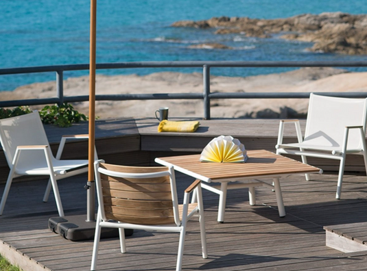 Fermob Pilotis teak outdoor armchair with low armrests, white cotton cushion, and sleek teak wood construction.