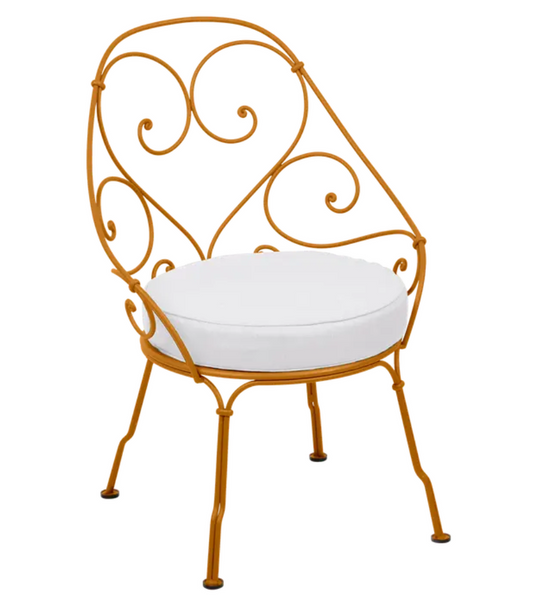 Off-white Fermob Cabriolet outdoor armchair with metal frame and ginger-colored cushion, stylish patio furniture.