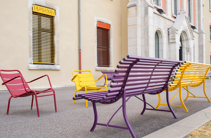 Load image into Gallery viewer, Fermob Louisiane outdoor folding bench with steel frame, designed for garden or patio seating, in a natural setting.
