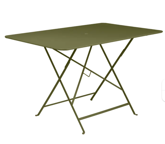Fermob Pesto foldable bistro table measuring 117 x 77 cm with metal outdoor design, shown in a natural outdoor setting.