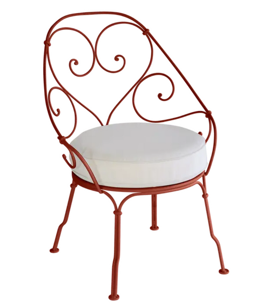 Red Ochre Fermob Cabriolet outdoor armchair with off-white cushions, metal frame, stylish outdoor furniture for gardens and patios.