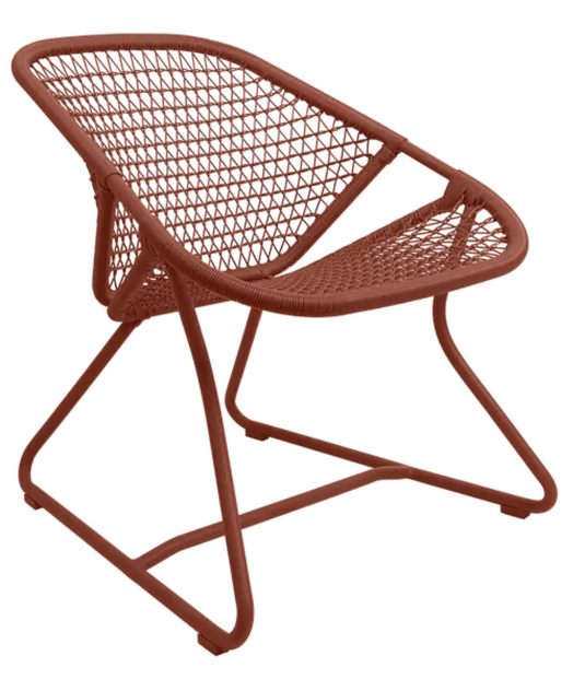 Red woven Fermob Sixties Low Armchair, stylish lounge chair with low armrests, suitable for restaurant or stylish indoor settings.