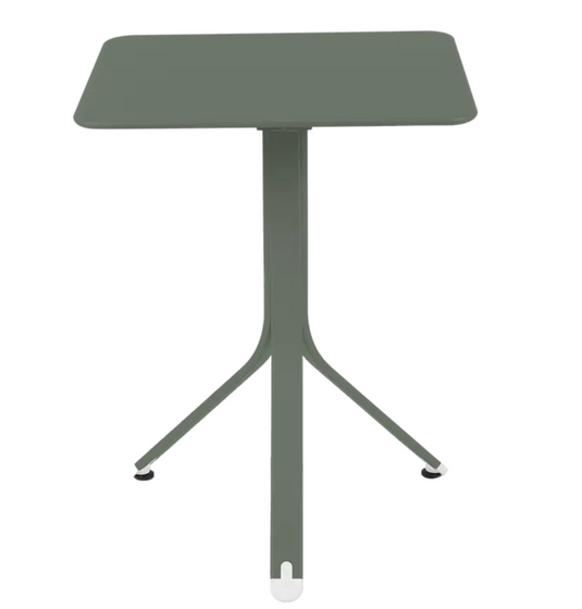 Fermob Rest'O folding outdoor table in metal, 57x57cm, shown in a small outdoor setting with a rosemary plant nearby