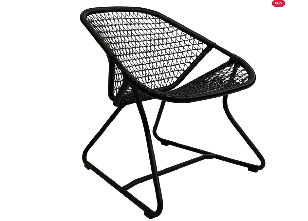 Woven Fermob Sixties Low Armchair in a lounge setting with a curved backrest and woven seat for relaxed seating.