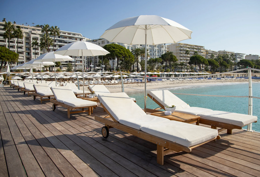 Fermob IBIZA teak outdoor sunlounger with a slatted design, positioned on a beach with a scenic Irish coastline in the background.