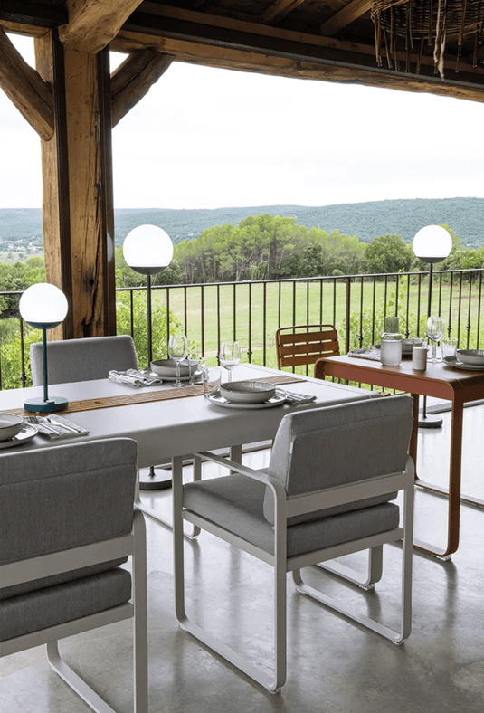 Fermob Bellevie outdoor dining armchair with a nutmeg grey toupet cushion and armrests, designed for comfortable outdoor seating.