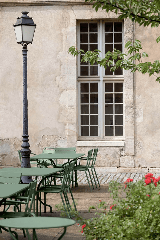 Fermob OPÉRA+ outdoor metal table with 67 cm diameter, suitable for patio or restaurant settings, shown on a patio surface.