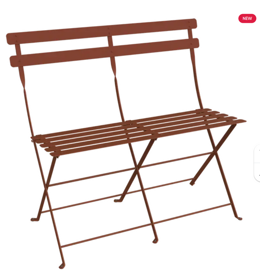 Red Fermob Bistro Two Seater Ottoman folding bench with wooden legs, designed for outdoor seating and versatile use.
